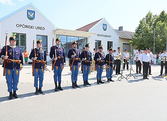 Eine Militärkapelle steht vor einem Gebäude namens Opcinski Ured mit einer Menschenmenge hinter ihnen.