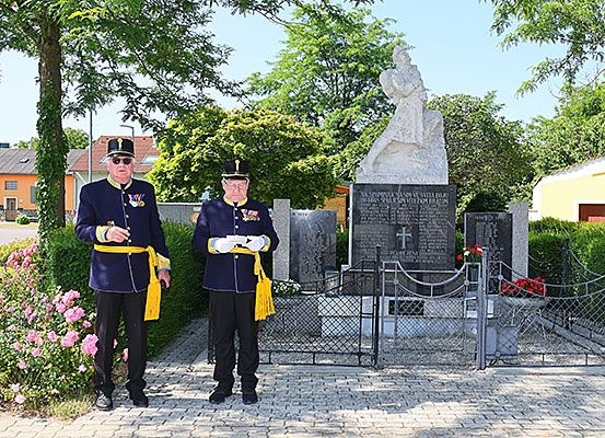 Zwei Männer in Militäruniformen stehen neben einer Gedenkstatue in einem Park. Das Denkmal ist von einem Zaun umgeben.