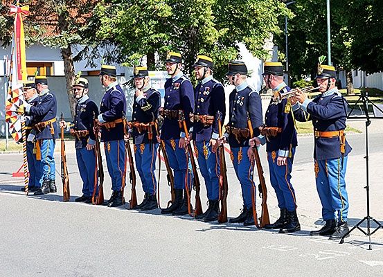 Soldaten in Uniform stehen in einer Reihe, halten Gewehre, mit einer Flagge und einem Trompeter im Vordergrund.