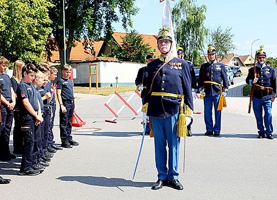Soldaten in Uniform stehen in einer Reihe mit einem Mann vor ihnen. Sie halten eine Flagge und ein Gewehr. Ein Junge hält eine Flagge.