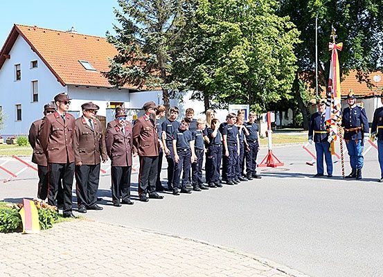 Eine Gruppe in Uniform steht im Freien in einer Reihe. Dahinter steht ein Haus mit einem Fahnenmast.
