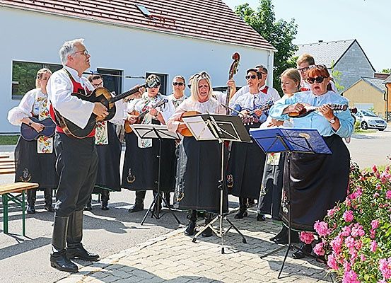 Eine Gruppe von Musikern in traditioneller Kleidung steht auf der Straße, spielt Gitarren und singt, während andere zusehen.