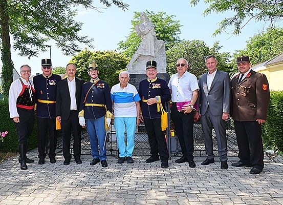 Eine Gruppe von Männern in verschiedenen Uniformen steht vor einer Statue auf einem Kopfsteinpflaster. Sie scheinen für ein Foto zu posieren.