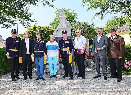 Eine Gruppe von Männern in Uniform und formeller Kleidung posiert für ein Foto vor einer Statue in einem Park.