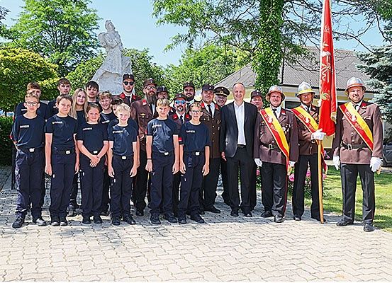 Eine Gruppe von Menschen, einschließlich Kinder, in Uniformen, steht vor einer Statue und einer Fahne.