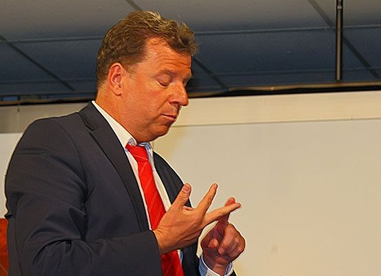Ein Mann in Anzug und roter Krawatte hält eine Rede. Er hat die Hände offen und schaut nach unten.