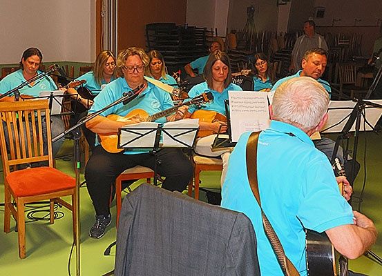 Eine Gruppe von Musikern in blauen Shirts spielt Gitarre, begleitet von einer Person in einem blauen Shirt, die Noten liest.