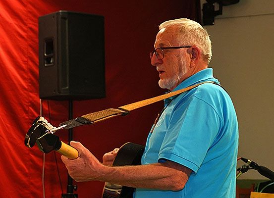 Ein älterer Mann spielt Gitarre, steht vor einem Mikrofon und einem Lautsprecher.