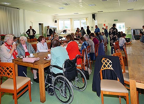 Eine Gruppe älterer Menschen sitzt um einen Tisch in einem Esszimmer. Eine Person ist im Rollstuhl.