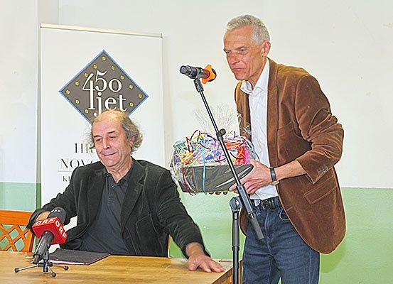 Zwei Männer stehen an einem Schreibtisch mit Mikrofonen. Einer hält einen Geschenkkorb. Hinter ihnen ist ein Banner mit '450 liet' darauf geschrieben.