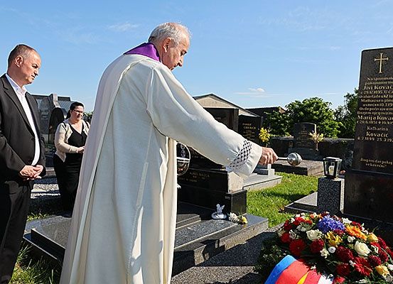 Ein Priester in einer weißen Robe legt eine Glocke auf einen Grabstein auf einem Friedhof.