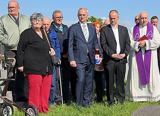 Eine Gruppe von Menschen, darunter ein Priester, steht auf einem Friedhof, möglicherweise bei einer Beerdigung.