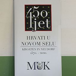 Poster zeigt '450 Jahre, Kroaten in Neudorf 1570-2020' mit einem Wappen darüber. Grüner und weißer Hintergrund.