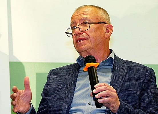 Ein Mann mit Brille und Anzug spricht in ein Mikrofon und zeigt mit der Hand.