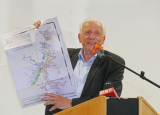 Ein älterer Mann hält eine Karte in der Hand und spricht an einem Rednerpult mit Mikrofon.