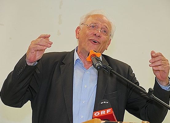 Ein älterer Mann in einem schwarzen Blazer und mit Brille hält eine Rede in ein Mikrofon. Er hat die Hände erhoben und scheint aufgeregt zu sein. Auf dem Mikrofon steht 'ORF'.
