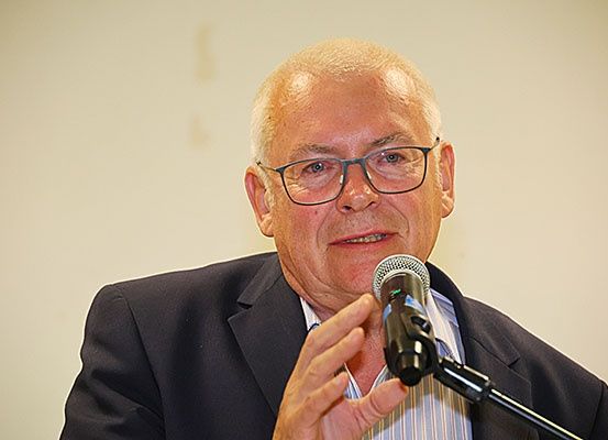 Ein älterer Mann mit Brille und Anzug spricht in ein Mikrofon und blickt nach rechts.