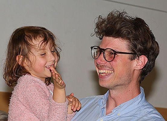 Ein junges Mädchen mit nassen Haaren lacht und hält sich die Finger vor den Mund. Ein Mann mit Brille lächelt sie an.