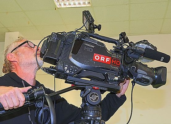 Ein Mann justiert eine Sony XDCAM HD Videokamera, hält sie mit beiden Händen und bläst in ihr Mikrofon.