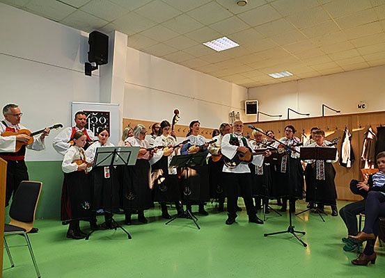 Eine Gruppe von Musikern spielt verschiedene Instrumente in einem Raum mit grünem Boden. Einige halten Gitarren, während andere Violinen haben. Einige Leute beobachten.