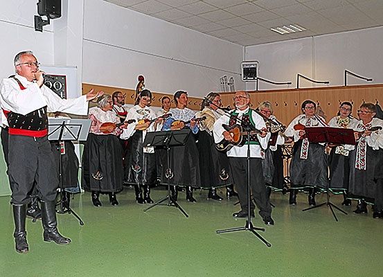 Eine Gruppe von Musikern tritt in einem Raum auf, wobei ein Mann in ein Mikrofon singt, während andere Gitarren und Violinen spielen.