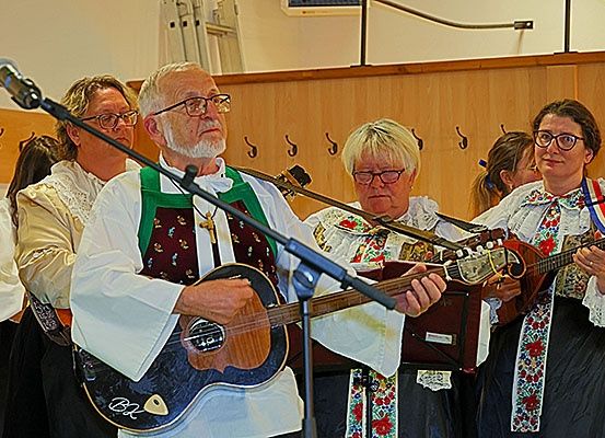 Eine Gruppe von Menschen spielt Gitarren in einem Raum, mit einem Mikrofon vor ihnen. Sie tragen traditionelle Kleidung.