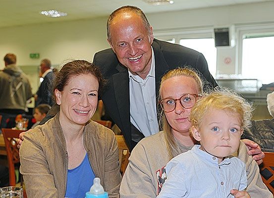 Eine Gruppe von Menschen posiert für ein Foto in einem Restaurant, wobei ein Mann und zwei Frauen zusammensitzen und ein Kind auf dem Schoß einer der Frauen sitzt.