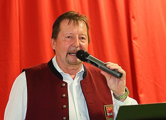 Ein Mann steht vor einem Mikrofon, hält es in der rechten Hand und scheint bei einer Veranstaltung zu singen.