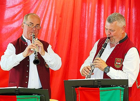 Zwei Männer in Westen spielen Klarinetten vor einem roten Vorhang, wahrscheinlich bei einer musikalischen Veranstaltung.