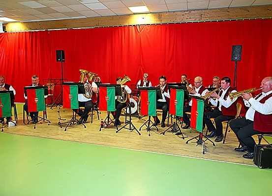 Ein Brass-Band spielt auf einer Bühne mit roten Vorhängen, trägt grüne und rote Uniformen und spielt Trompeten und Tuben.