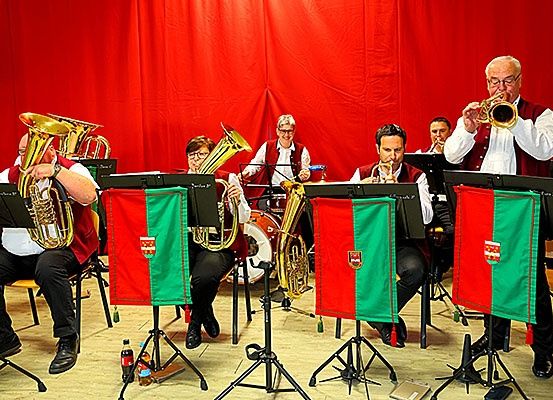 Eine Brass-Band spielt auf der Bühne mit roten Hintergründen und hält Blechblasinstrumente.