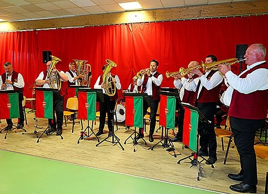 Ein Brass-Band spielt auf der Bühne mit rotem Hintergrund, Musiker spielen Trompeten, Tuben und ein Schlagzeug.