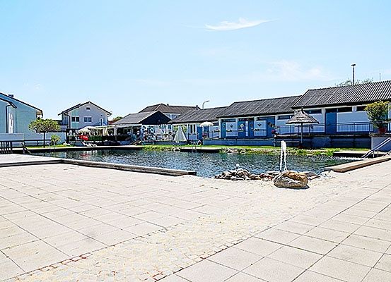 Ein Außenbereich mit einem großen Schwimmbecken, umgeben von Gebäuden mit blauen Wänden und Dächern, und einigen Bäumen.