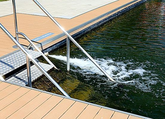 Ein Metallgeländer auf einem Holzsteg in der Nähe eines Schwimmbeckens mit fließendem Wasser.