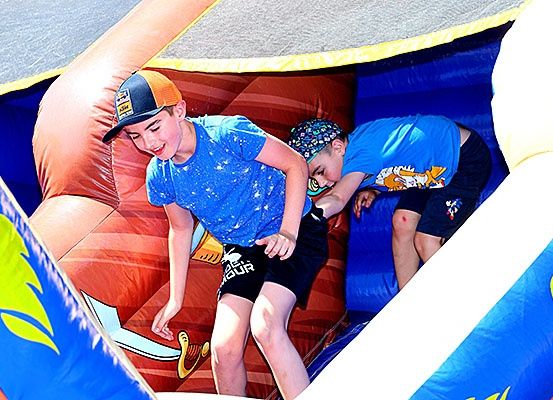 Zwei Jungen spielen in einem aufblasbaren Hindernisparcours. Ein Junge klettert und der andere liegt. Sie tragen beide blaue T-Shirts.