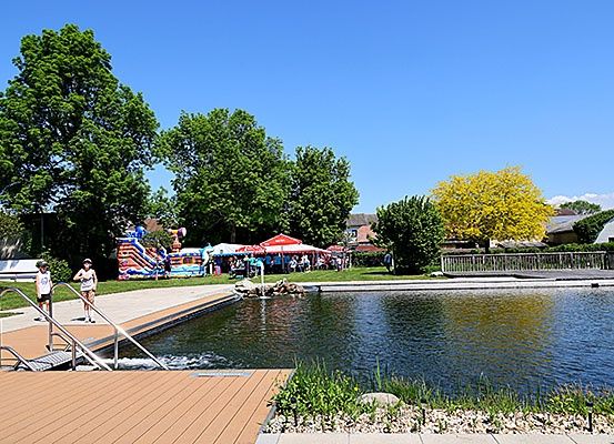 Ein Park mit einem großen Teich, Bäumen und Menschen, die in der Nähe einer Wasserrutsche stehen.