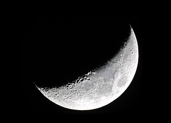 Ein Mondsichel am Nachthimmel, beleuchtet von der Sonne. Der Mond erscheint hell mit sichtbaren Kratern.