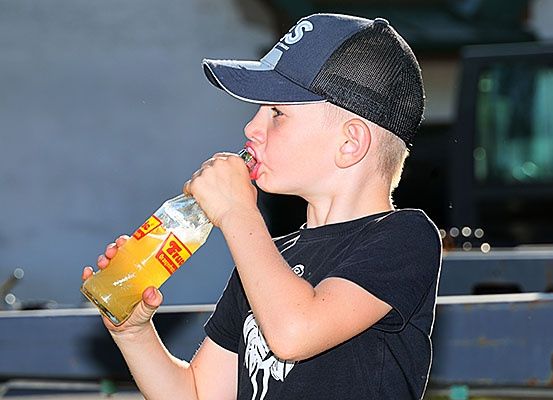 Ein junger Junge trinkt eine Flasche eines gelben Getränks mit einem Verschluss. Er trägt ein schwarzes T-Shirt und eine marineblaue Baseballkappe.