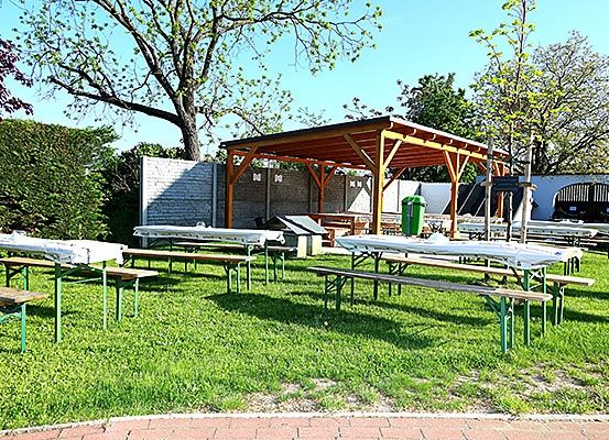 Eine Outdoor-Sitzfläche mit Picknicktischen, Bänken und einem Pavillon. Der Rasen ist grün und es gibt Bäume im Hintergrund.