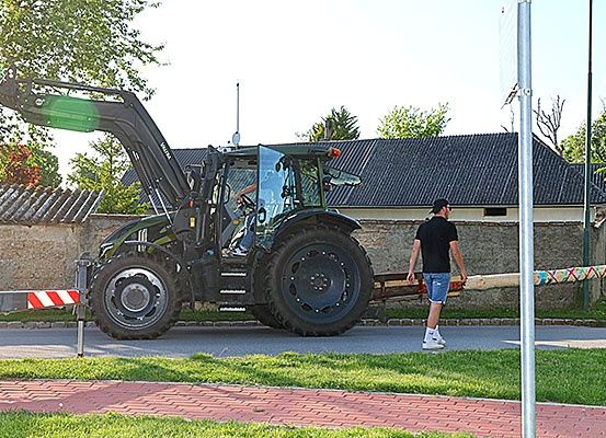 Ein Mann geht neben einem geparkten Traktor am Straßenrand. Ein langer Holzbalken ist am Traktor befestigt.