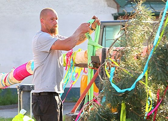 Ein Mann in einem grauen T-Shirt und schwarzen Hosen schmückt einen Baum mit bunten Bändern.