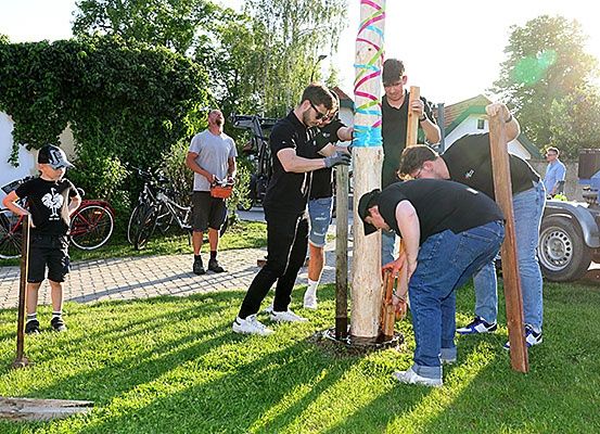 Mehrere Männer arbeiten gemeinsam daran, einen Pfahl zu reparieren, während andere zusehen, und ein Kind steht mit einem Fahrrad in der Nähe.