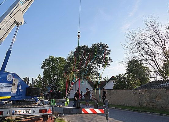 Ein Kran hebt bunte Bänder in die Luft in der Nähe einer Straße, an der Menschen stehen.