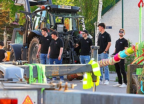 Fünf Männer stehen in der Nähe eines großen Traktors, wobei eine Person im Vordergrund eine Warnweste trägt. Hinter ihnen schaut ein Kind auf den Traktor.