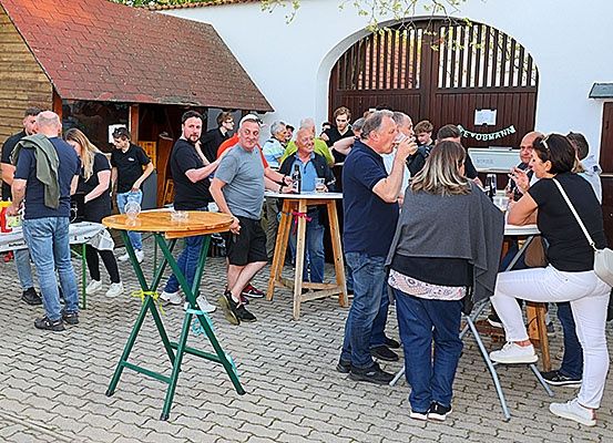 Eine Gruppe von Menschen versammelt sich im Freien um Tische, einige sitzen und andere stehen. Im Hintergrund ist ein Schild mit der Aufschrift 'EvoBahn' zu sehen.