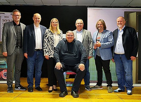 Eine Gruppe von Menschen, darunter Männer und Frauen, steht auf einer Bühne, lächelt und posiert für ein Foto.