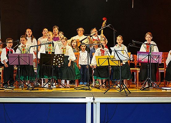 Ein Kinderchor tritt auf der Bühne auf, singt und steht um Notenständer mit Instrumenten und Mikrofonen herum.