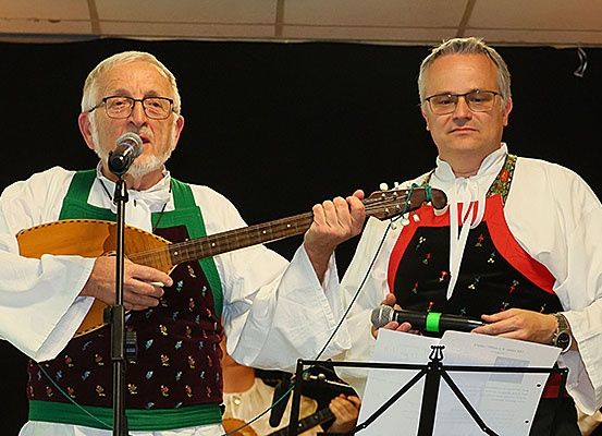 Zwei Männer treten auf der Bühne auf, einer spielt Gitarre und der andere hält ein Mikrofon. Sie tragen beide traditionelle Kleidung.
