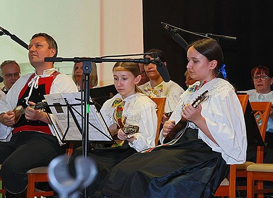 Eine Gruppe von Musikern tritt auf der Bühne auf, wobei zwei Mädchen Gitarre spielen, ein Mann neben ihnen sitzt und eine Frau hinter ihnen steht. Sie tragen alle traditionelle Kleidung.