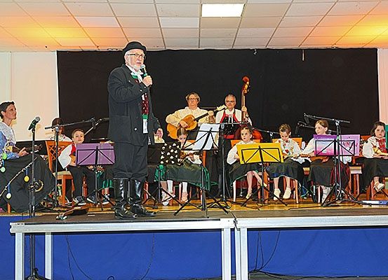 Eine Gruppe von Musikern steht auf der Bühne und spielt. Sie haben verschiedene Instrumente wie Gitarren und Celli. Ein Mann steht mit einem Mikrofon, wahrscheinlich singt er. Die Bühne hat einen blauen Hintergrund.